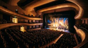 A cinematic, high-angle wide shot of a modern Norwegian cultural venue bathed in warm stage lighting