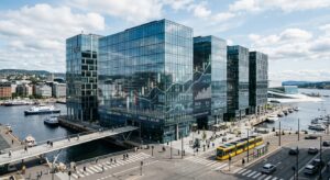 A professional editorial photograph of a modern Norwegian business district with blurred financial c